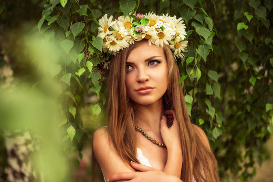 young beautiful woman outdoor in a birchwood wearing wreth of daisy