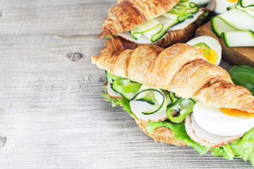 Chicken ham and  egg breakfast sandwich on a croissant on a rustic wooden board. Selective focus.