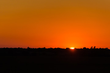 Calm hot sunset on the background of horizontal silhouette forests and villages