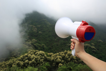 hand hold loudspeaker to blue sky on mountain peak