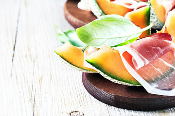 Melon and prosciutto on a dark wooden board with free text space, selective focus