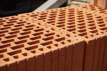 
Row of bricks in red and orange color with the inner holes in the shape of honeycomb on the construction site