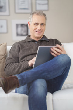 älterer mann sitzt auf dem sofa und liest am tablet