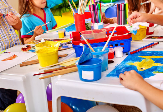 Group Of Children Hands  Painting On Paper At Table  In  Kindergarten . Paint Lesson.