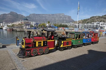 Cercles muraux Afrique du Sud CAPE TOWN WATERFRONT SOUTH AFRICA - APRIL 2016 - Man in uniform carrying a red flag with a children's train ride around the harbor area of the V&A Waterfront. A major attraction in Cape Town