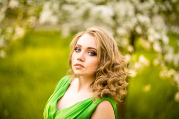 beautiful young blond woman standing beside a blossoming Apple tree