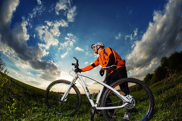 Fototapeta na wymiar biker in orange jersey riding on green summer field
