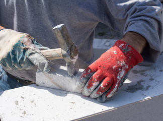 Worker with old and dirty working gloves hitting with hammer white concrete block, small pieces of...