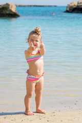 Obraz premium Little baby girl showing thumbs up on the beach.