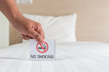 Hand holding NO SMOKING sign on the bed in hotel room