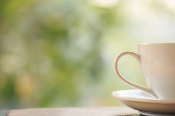 White coffee cup on table in garden with blur light bokeh