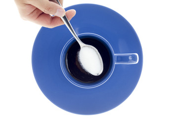 cropped view of a human hand with spoon of sugar over coffee cup.