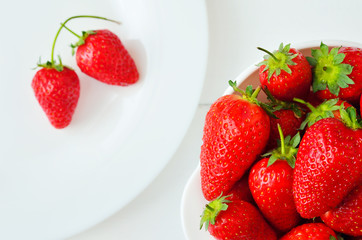 Ripe strawberries in a white bowl and on a white plate. Strawberry on a white background