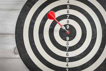Red dart arrow hitting in the target center of dartboard