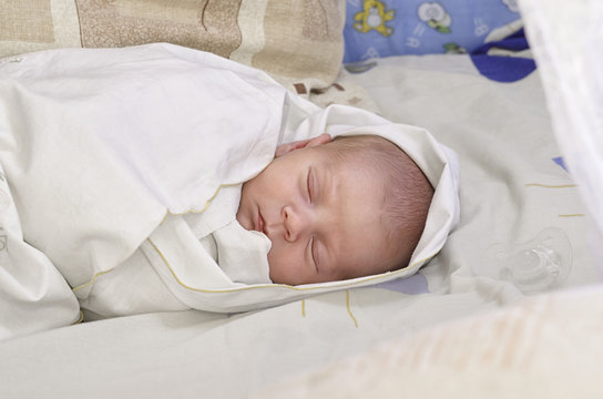 Новорожденный  ребенок спит в своей кроватке под одеялом.