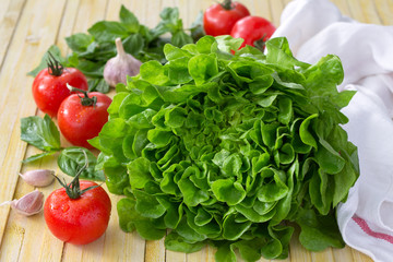 Fresh lettuce, tomato, basil and garlic for a light summer salad on a wooden surface, selective focus