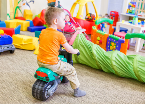 boy sitting on a toy motorcycle. child playing in a room with a lot of scattered toys