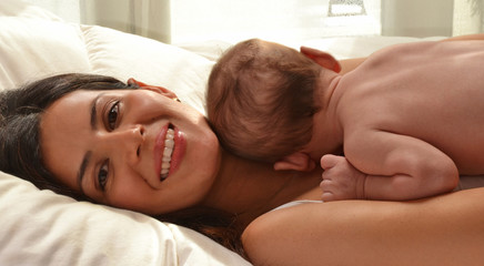 Obraz na płótnie Canvas Madre latina feliz compartiendo con su bebe en la cama jugando.