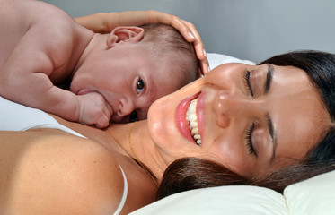 Madre latina feliz compartiendo con su bebe en la cama jugando.