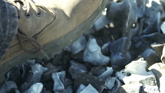 Close up shot of an anonymous person stepping in and moving around burned bones and ashes with a boot.