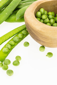 Fresh green pea pods and peas in wooden bowl, on white background