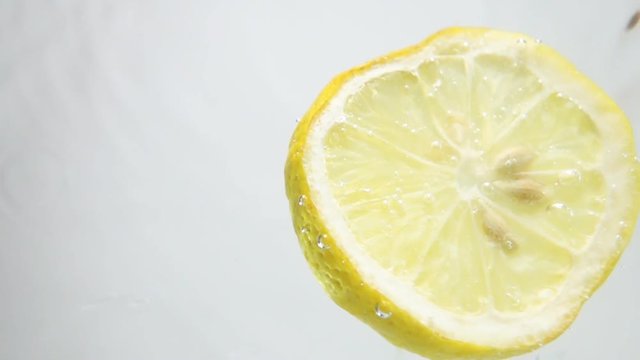 Round fresh lemon slice plunging into the transparent water  with explosive stunning splash, breaking the surface of liquid. Underwater high-speed slow motion shot on white background isolated. Camera