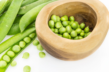 Fresh green pea pods and peas in wooden bowl, on white background