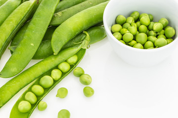 Fresh green pea pods and peas in bowl, on white background