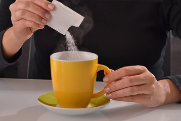 Agregando sobre de azúcar a la taza de cafe.
