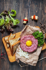 Beef tartare with bread and fresh onion on a wooden background