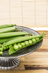 Fresh green pea pods in oriental dish, on wooden surface