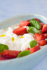 Creamy stracciatella with strawberries, basil and olive oil. Selective focus.
