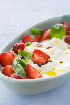 Creamy stracciatella with strawberries, basil, olive oil and balsamic vinegar. Selective focus.