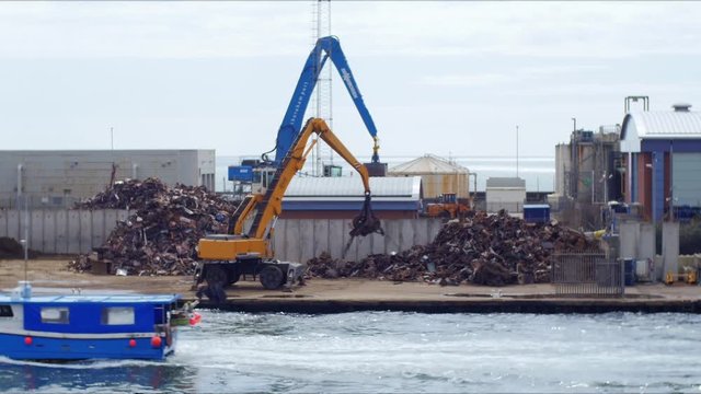 Crane arranging iron waste on an industrial site by the sea