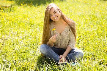 the portrait of the beautiful young woman with long hair with a flower sits on a grass in park
