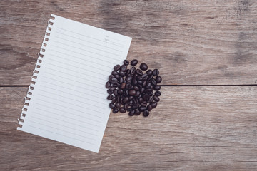 Coffee beans and and lined paper on wooden table top view