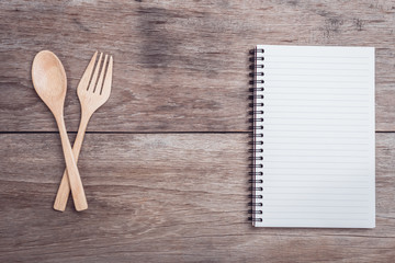 Wooden spoon, fork and lined paper on wooden table top view