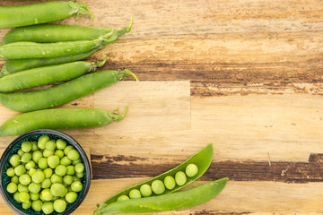 Fresh green peas in bowl and pea pods, on wooden surface