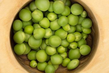 Fresh green peas in wooden bowl closeup background