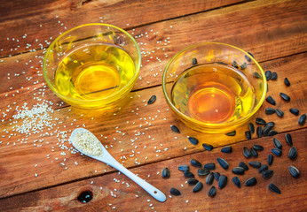 sesame and sunflower oil in glass bowls and seeds in a white spoon and on the wooden background