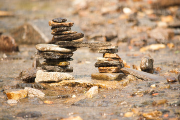 Zen tower bridge of different coloured stones in a shallow stream in the rain
