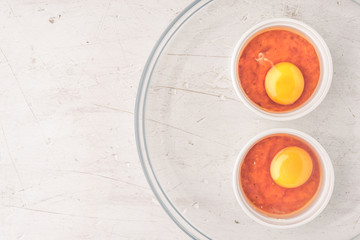 Raw eggs with tomatoes in the ramekins on the white  wooden table top view