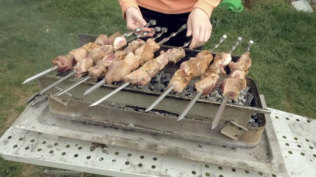 Girl cooks barbeque skewers with meat on hot coal ember brazier Outdoors picnic concept. 4K UHD video footage.