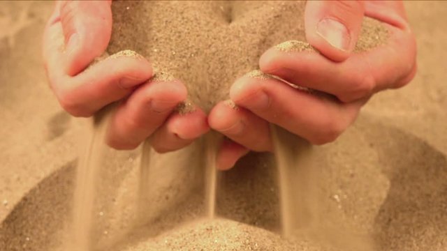 Handful of dry desert sand pouring through fingers, man holding pile of hot sandy dust