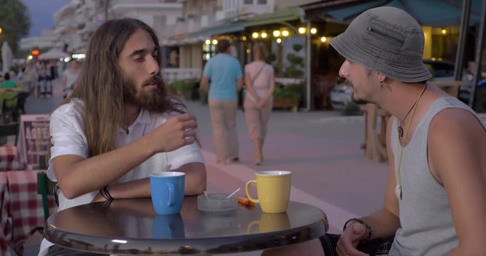 Old chaps having drinks and talking in street cafe in resort town in the evening