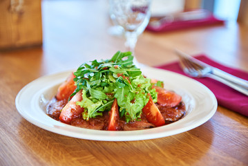 Salad with arugula leaves, fried meat and tomato on table