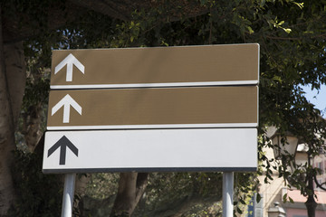 Cartelli di indicazioni di colore bianco e marrone con sfondo alberi in contesto cittadino