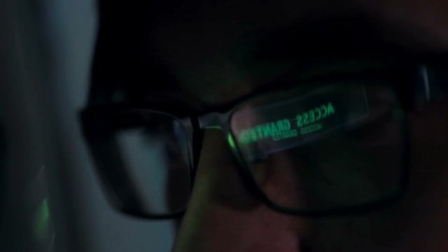 Computer Code Scrolling reflected in hackers glasses.