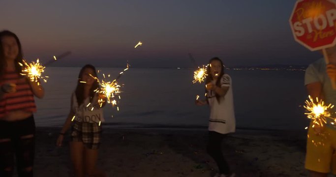 Steadicam shot of some people having fun during celebration on the beach. Night party with dancing and sparklers