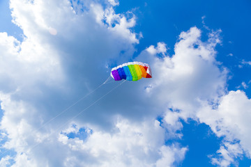 rainbow colored child's kite on blue sky with clouds
